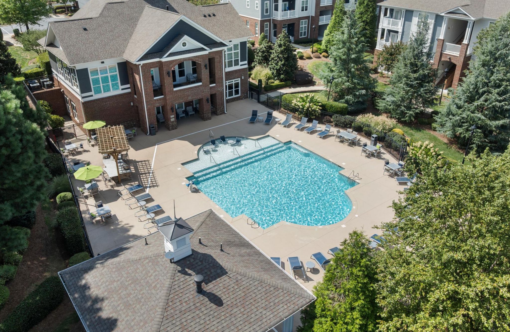 Aerial view of the Residences at Brookline apartment complex pool, surrounded by lounge chairs, umbrellas, and trees.