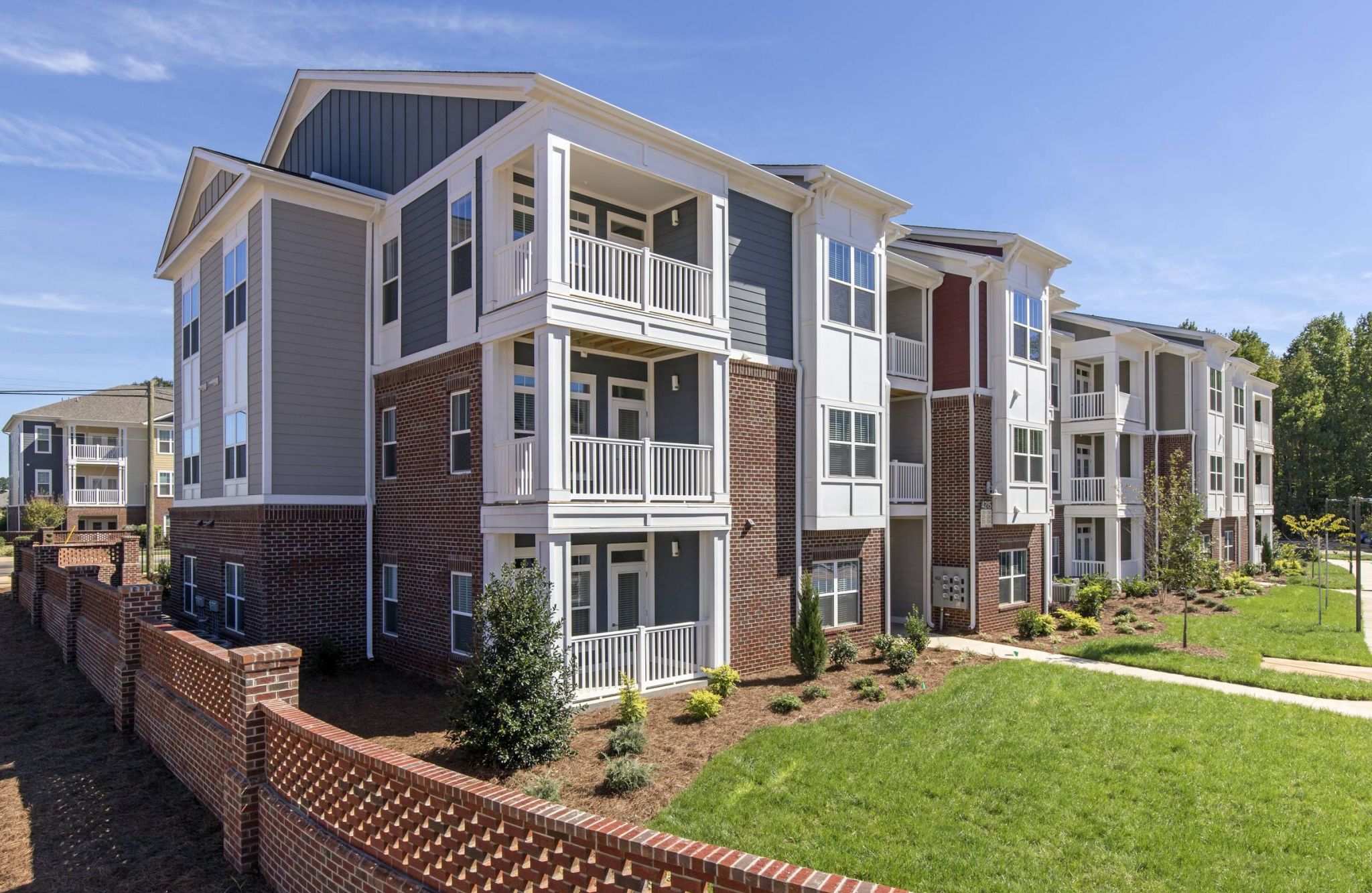 Modern three-story apartment building with balconies and red brick exterior, located in Proximity Northlake, features a landscaped lawn.