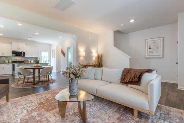 Bright living room at The Bend at Cramerton Mills with a white sofa, glass coffee table, and modern neutral decor open to kitchen and dining.