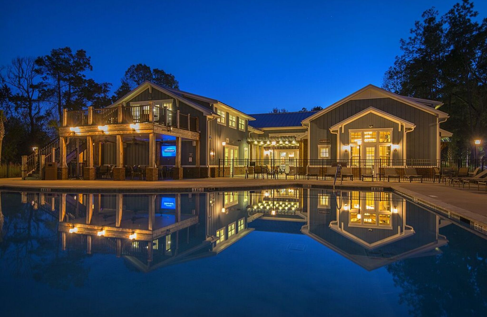 A large, illuminated building reflects on a still pool at night, surrounded by trees under a deep blue sky.