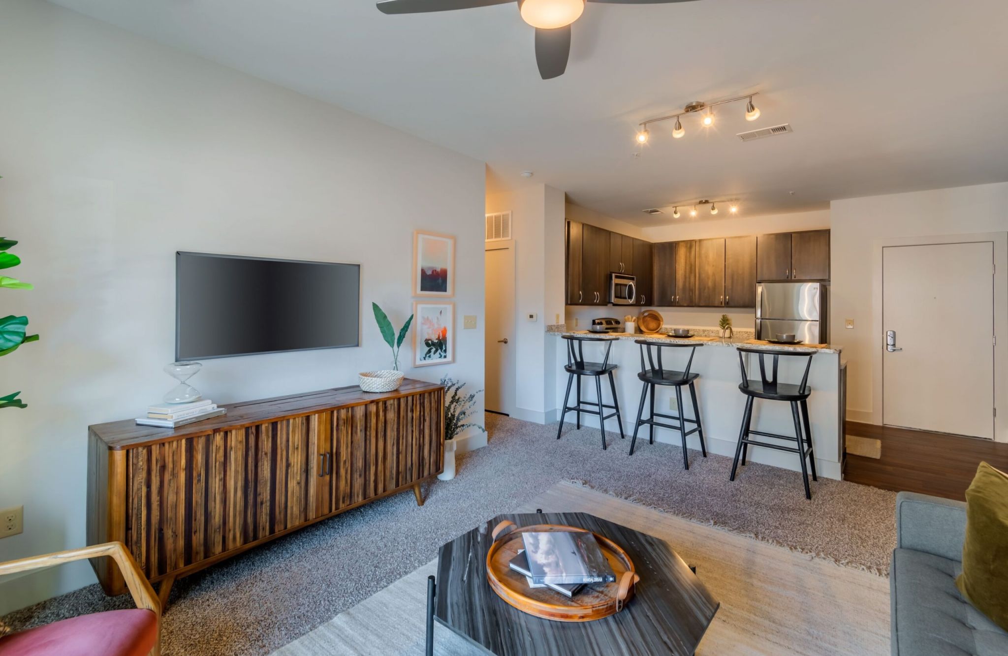 Modern living room at 927 West features wooden furniture, a wall-mounted TV, and a kitchen with barstools in the background.