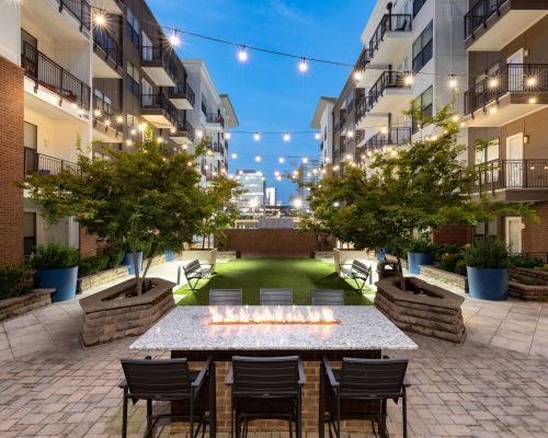 The modern courtyard at 1505 Demonbreun features string lights, a long fire pit table, and trees in planters.