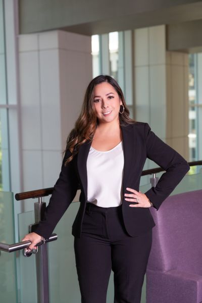 Woman in a black suit and white blouse stands confidently by a railing in a modern office building.