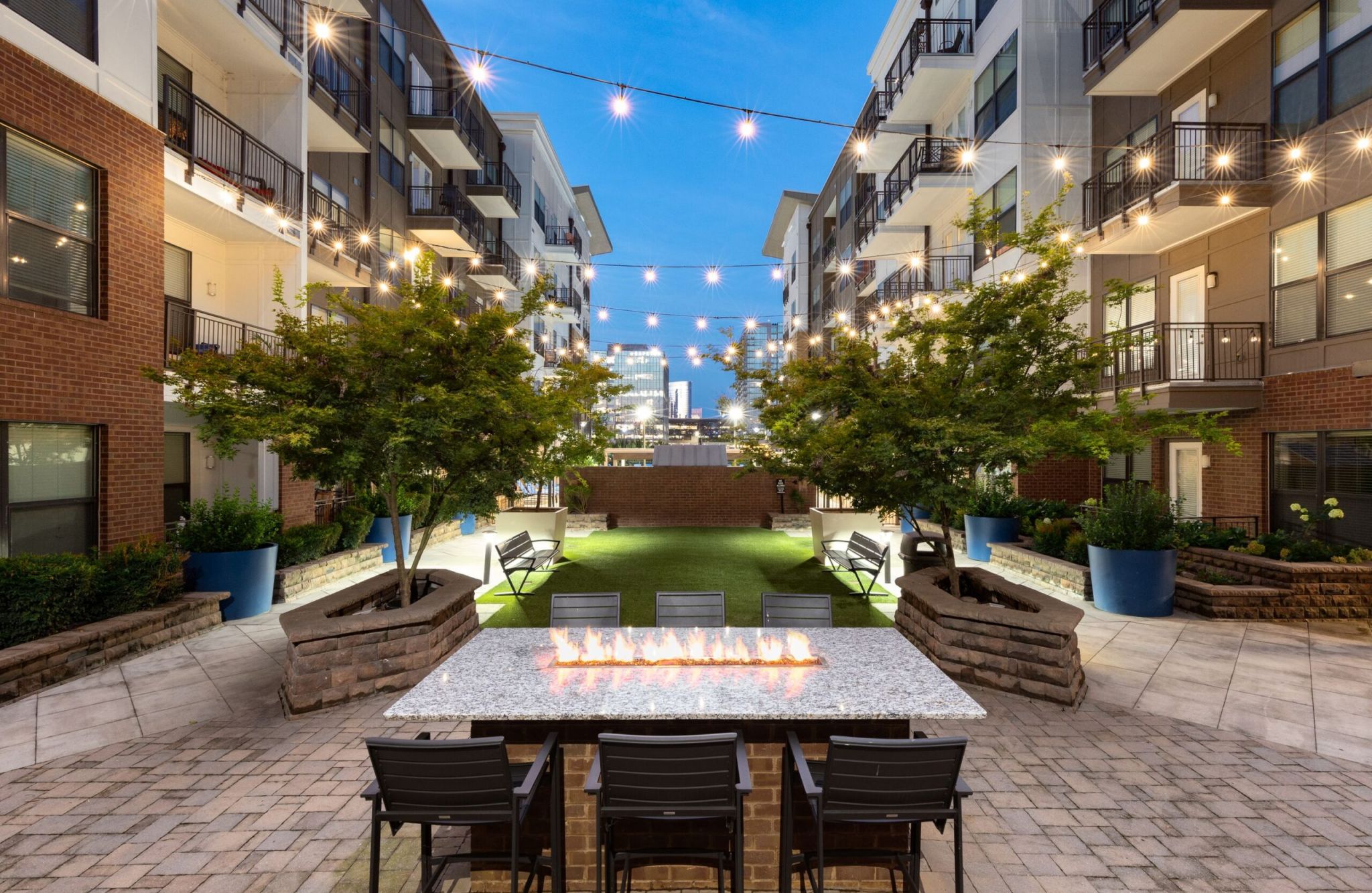 The modern courtyard at 1505 Demonbreun features string lights, a long fire pit table, and trees in planters.