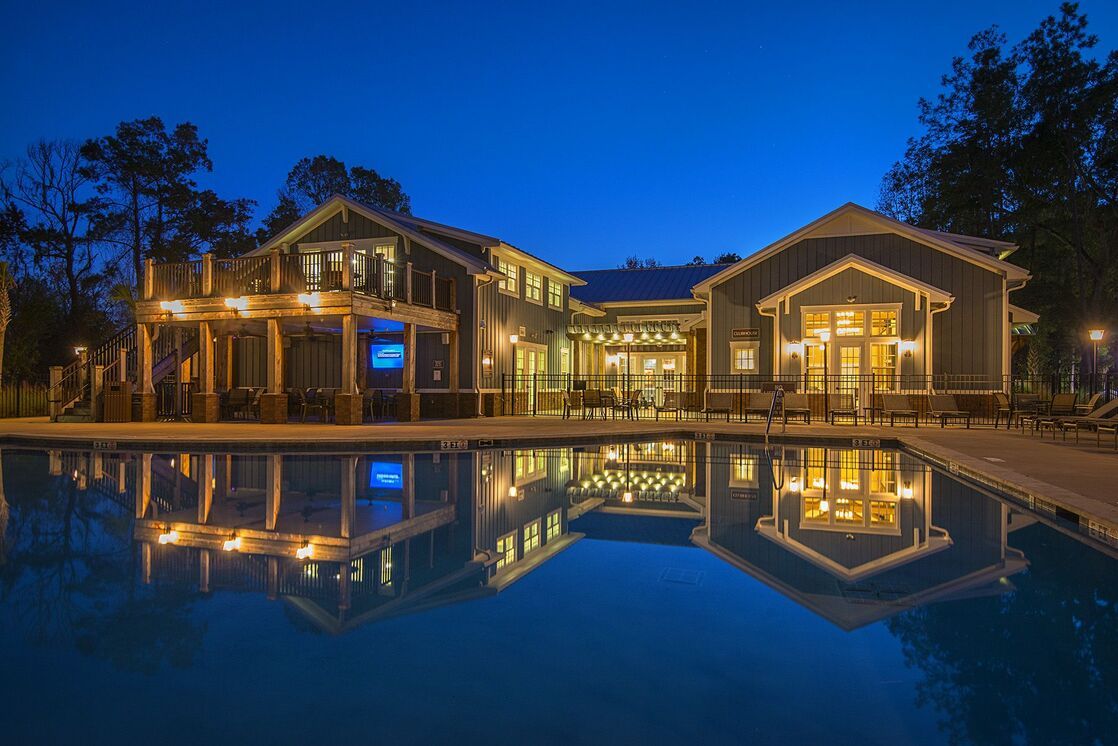 A large, illuminated building reflects on a still pool at night, surrounded by trees under a deep blue sky.