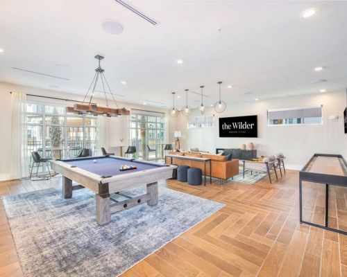 Modern recreation room with pool table, shuffleboard, and lounge area featuring a sign reading "the Wilder.