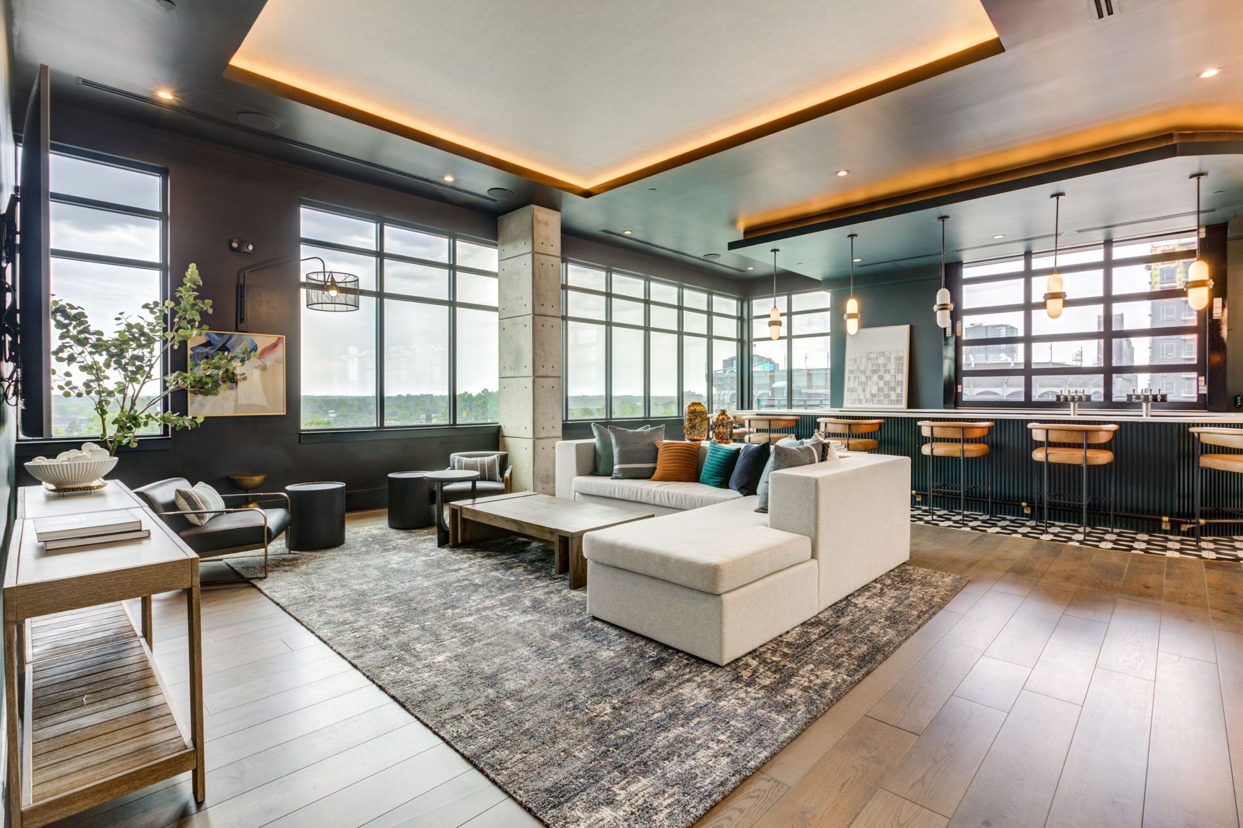 Modern lounge by Vest Residential with large windows, sectional sofa, bar area with stools, and stylish lighting on a hardwood floor.