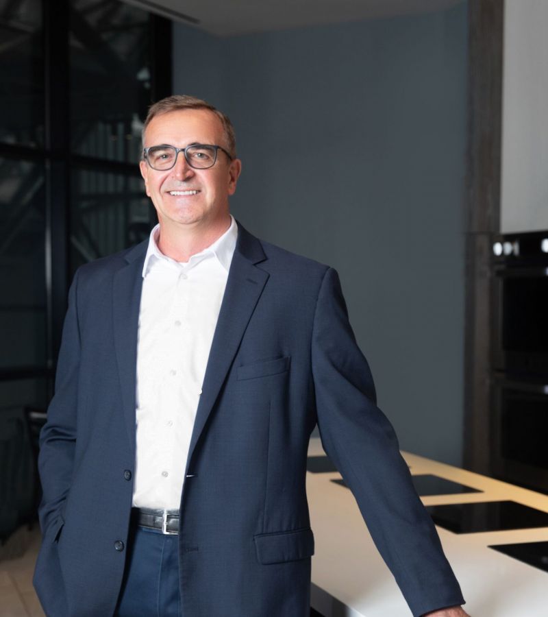 Smiling man in a suit stands next to a modern kitchen counter.
