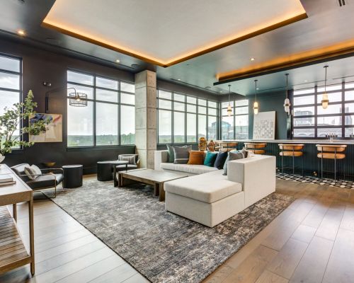 Modern open-concept living space with gray sectional sofa, bar area, large windows, and decorative lighting.