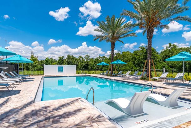 A sunny Southside Quarter outdoor swimming pool surrounded by lounge chairs, umbrellas, and palm trees under a blue sky.