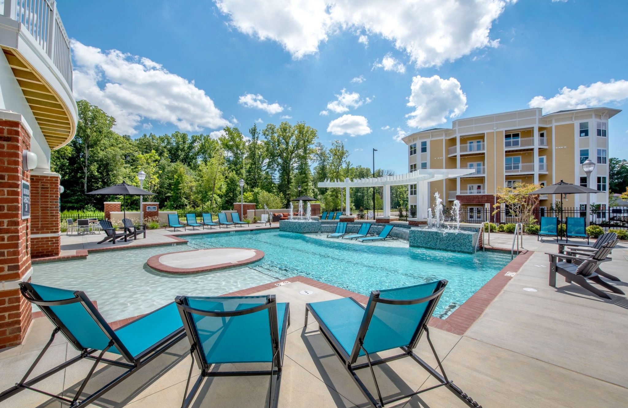 Outdoor pool area at Quarterpath with lounge chairs, umbrellas, and a modern building in the background under a partly cloudy sky.