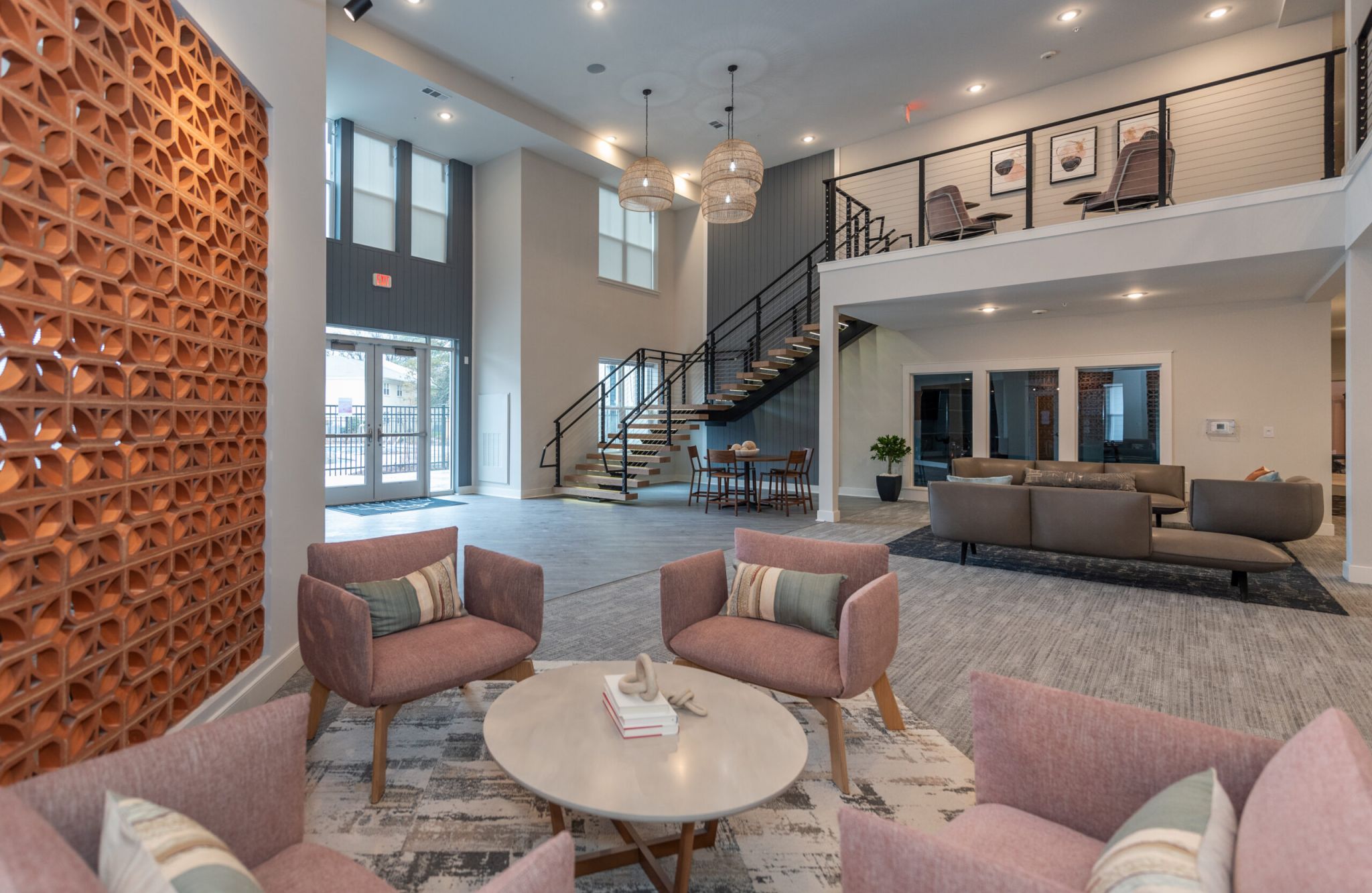 Modern lobby in Virginia Beach with pink chairs, round table, open staircase, sofas, balcony, and large windows letting in natural light.
