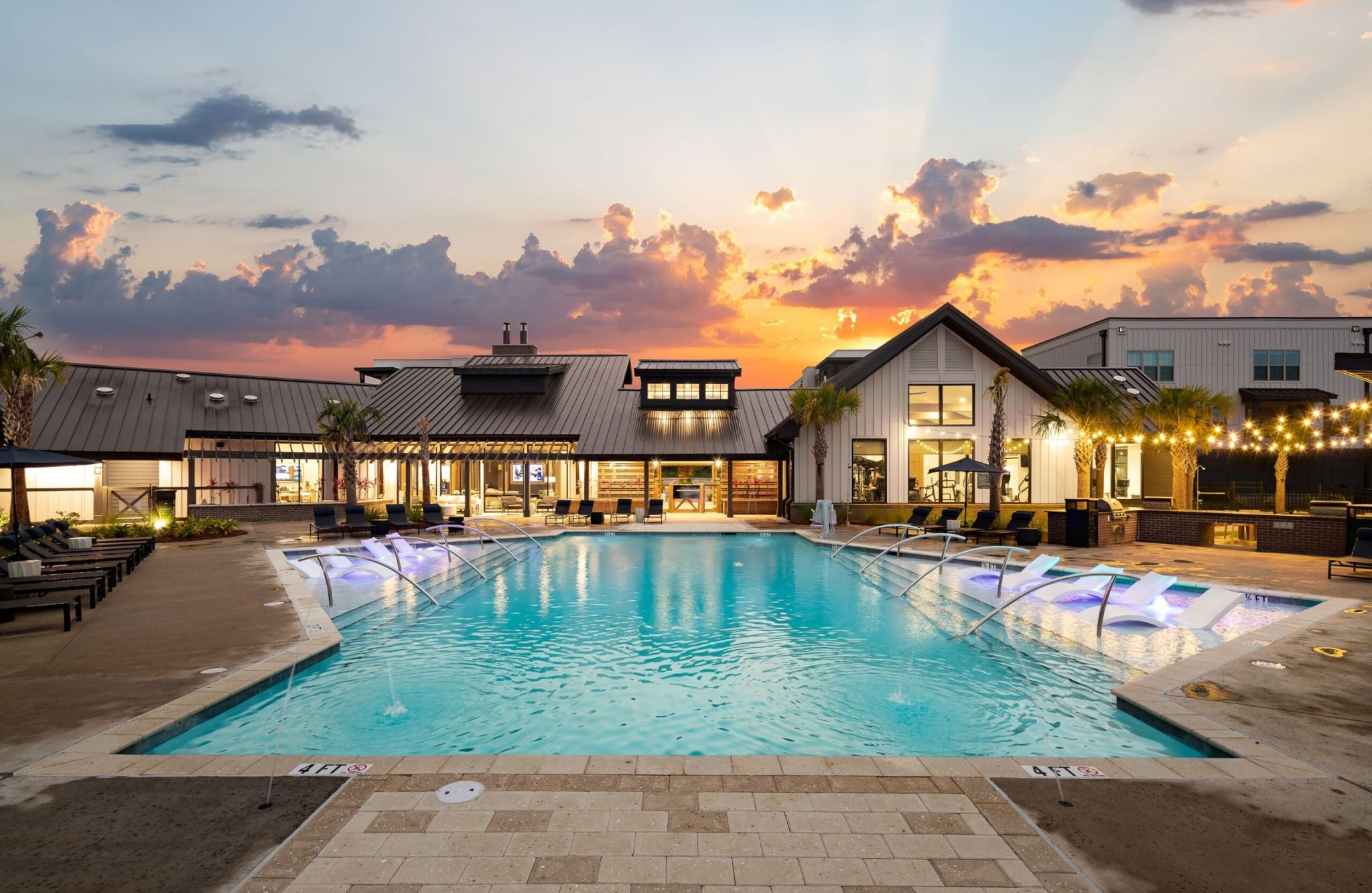 Outdoor pool area with loungers and modern buildings at sunset.