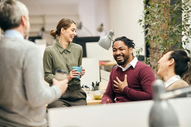 Four colleagues chatting and laughing in a modern office setting.