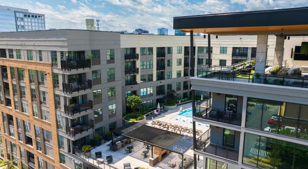 Aerial view of modern apartment complex with courtyard pool and balconies under a blue sky.