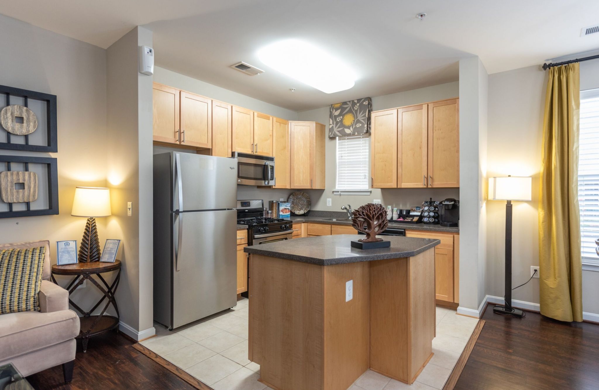 Modern kitchen with wood cabinets, stainless steel appliances, and a center island. Cozy living area visible on the left at Potomac Square Commons.