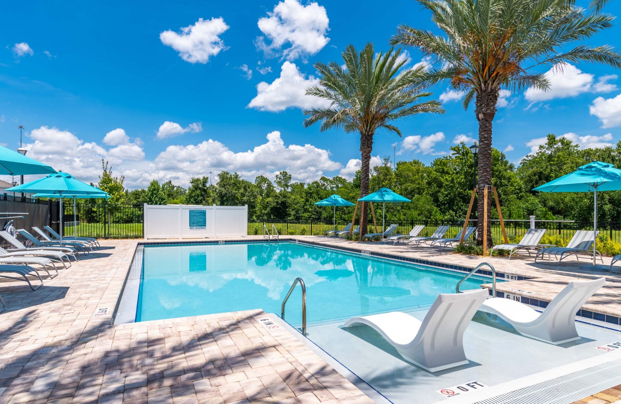 A sunny Southside Quarter outdoor swimming pool surrounded by lounge chairs, umbrellas, and palm trees under a blue sky.