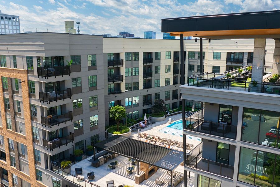 Aerial view of modern apartment complex with courtyard pool and balconies under a blue sky.