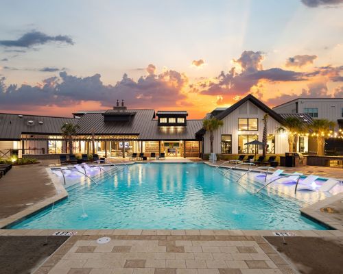 Outdoor pool area with loungers and modern buildings at sunset.
