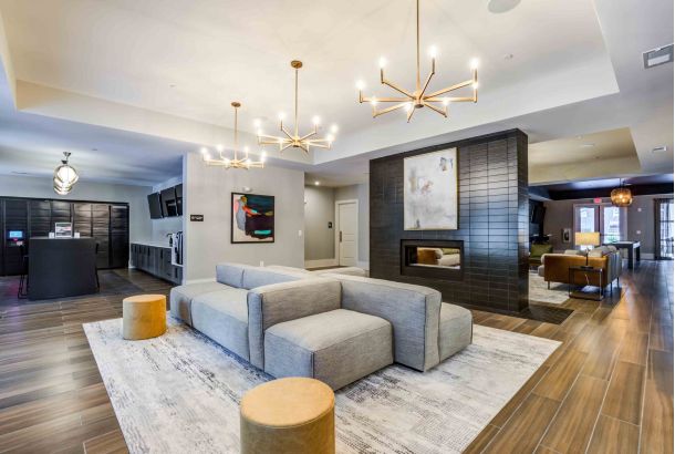 Modern Woodside Eleven lounge with gray couches, chandeliers, artwork, and wooden flooring. Cozy ambiance enhanced by the fireplace.