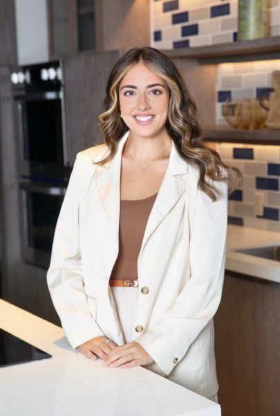 Smiling woman in a cream blazer standing in a modern kitchen.