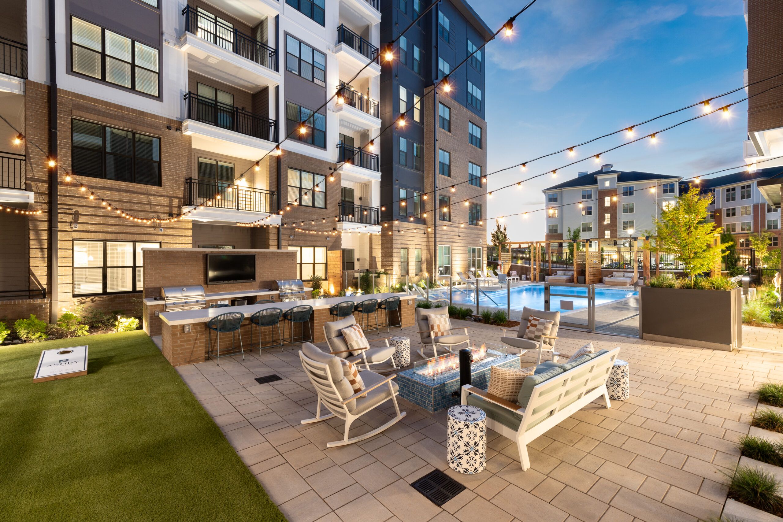 Twin Lakes apartment courtyard with string lights, seating, fire pit, and pool at dusk.