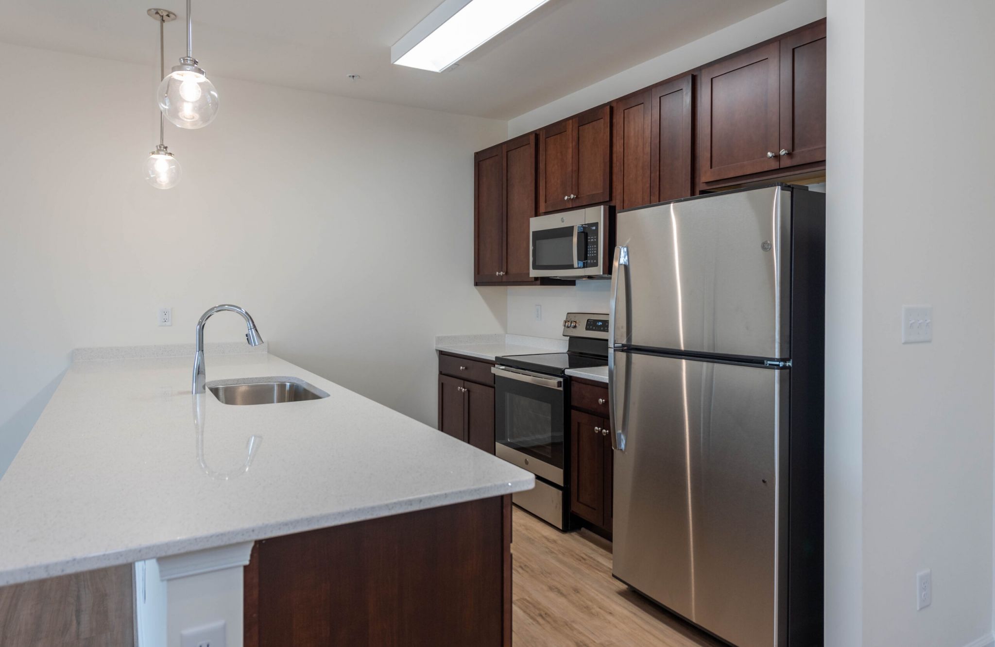 Modern kitchen at Magnolia Chase with dark wood cabinets, stainless steel appliances, and a large island with pendant lights.