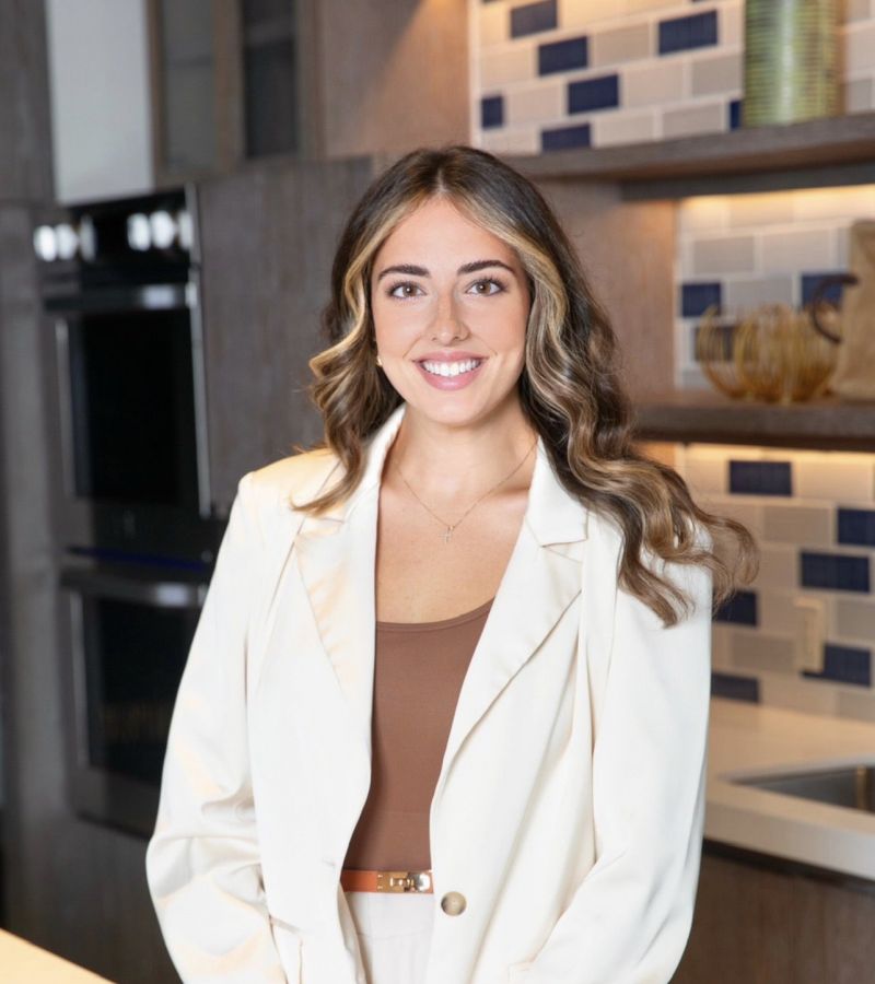 Smiling woman in a cream blazer standing in a modern kitchen.