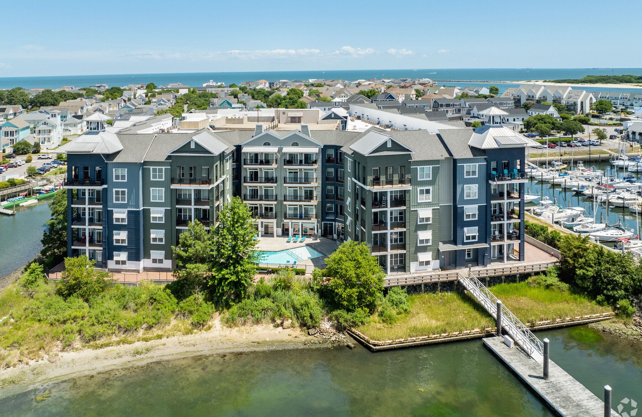 A modern Marina Apartments complex with balconies, pool, and East Beach Marina views, surrounded by lush greenery and docks.