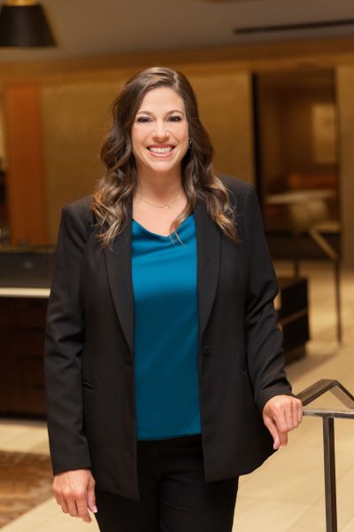 Woman in a black blazer and blue top smiling in an office setting.