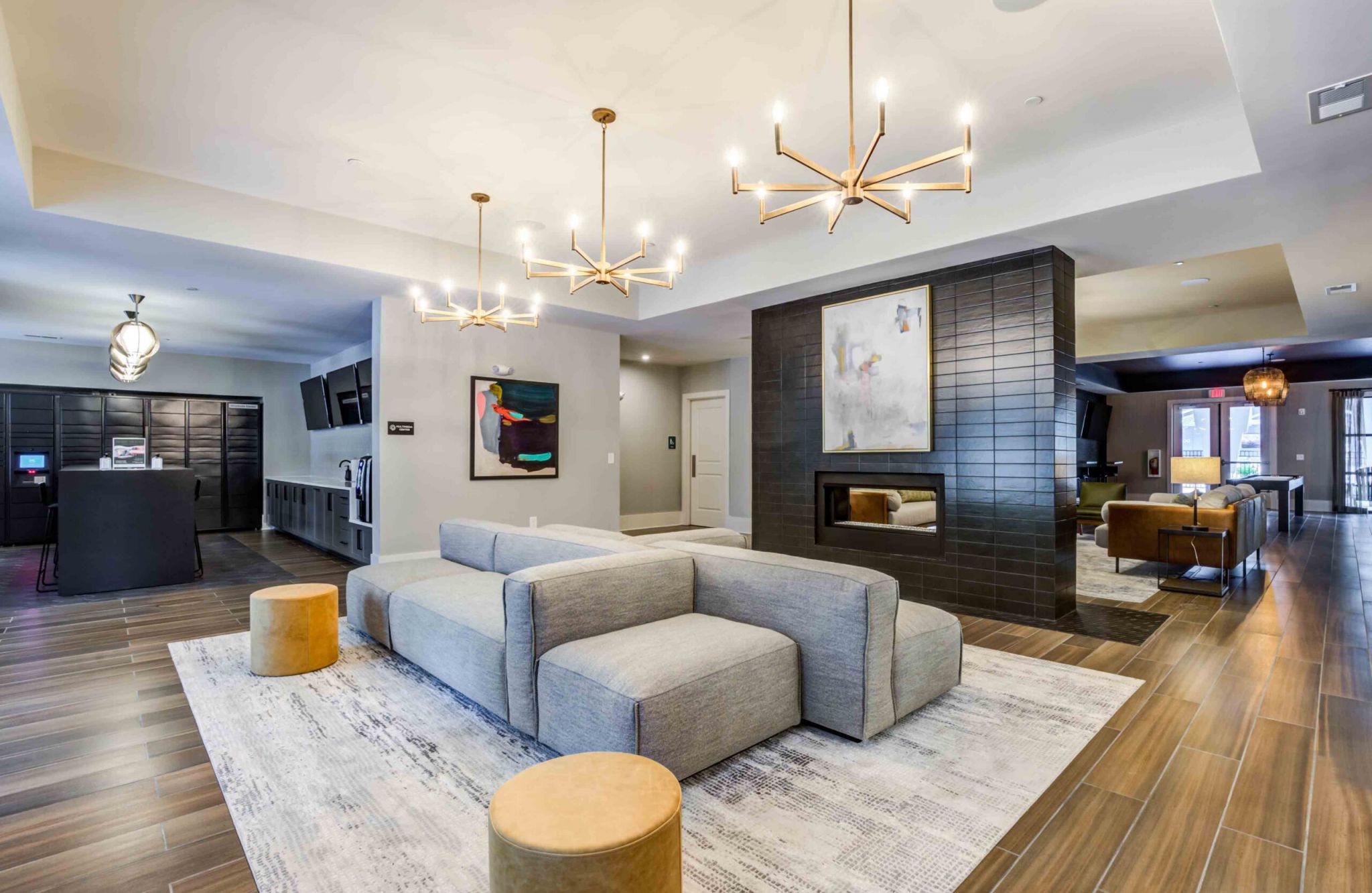 Modern Woodside Eleven lounge with gray couches, chandeliers, artwork, and wooden flooring. Cozy ambiance enhanced by the fireplace.