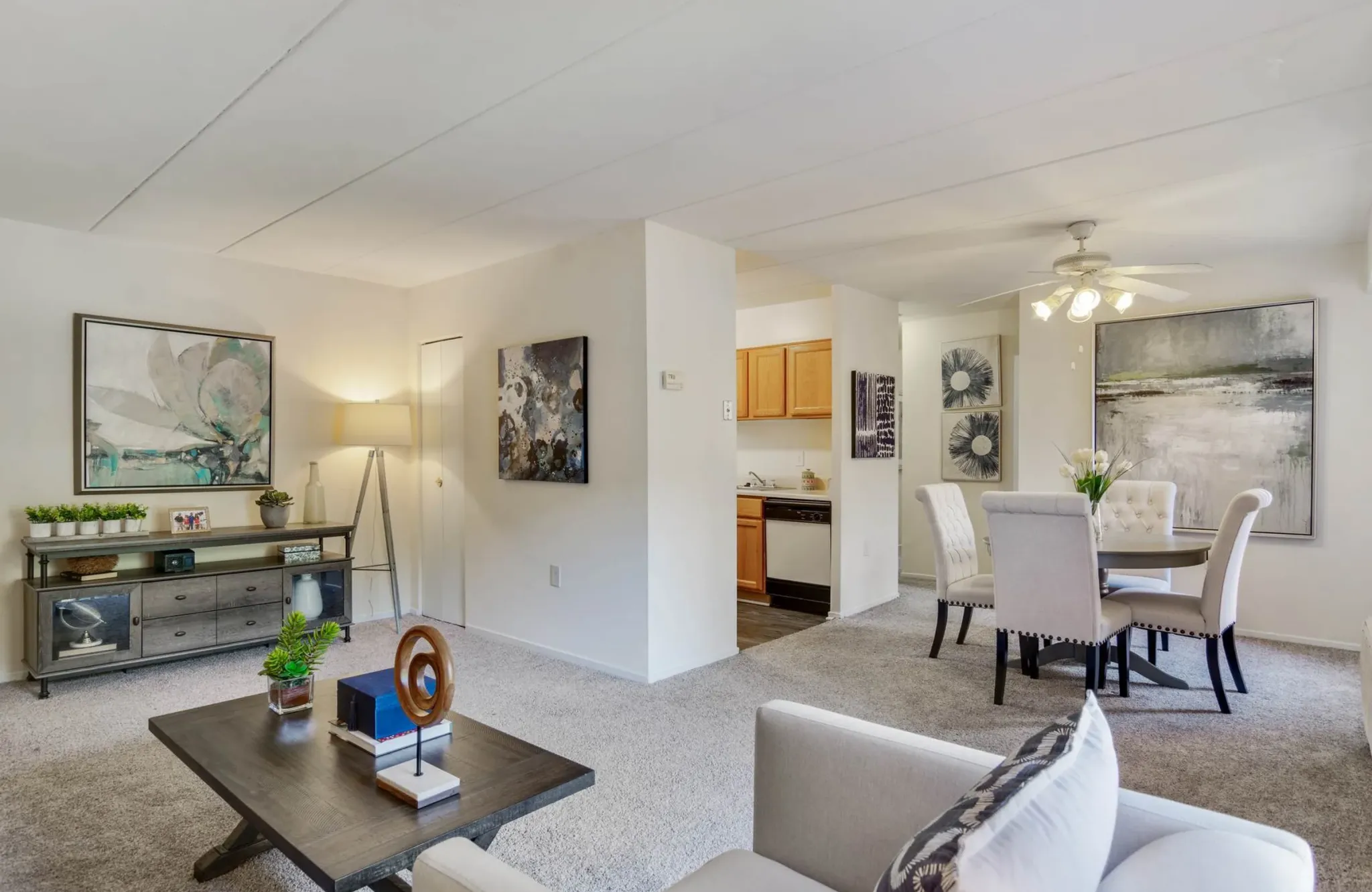 Modern living and dining area with neutral tones, wall art, and a small kitchen visible—perfect for stylish apartment rentals.