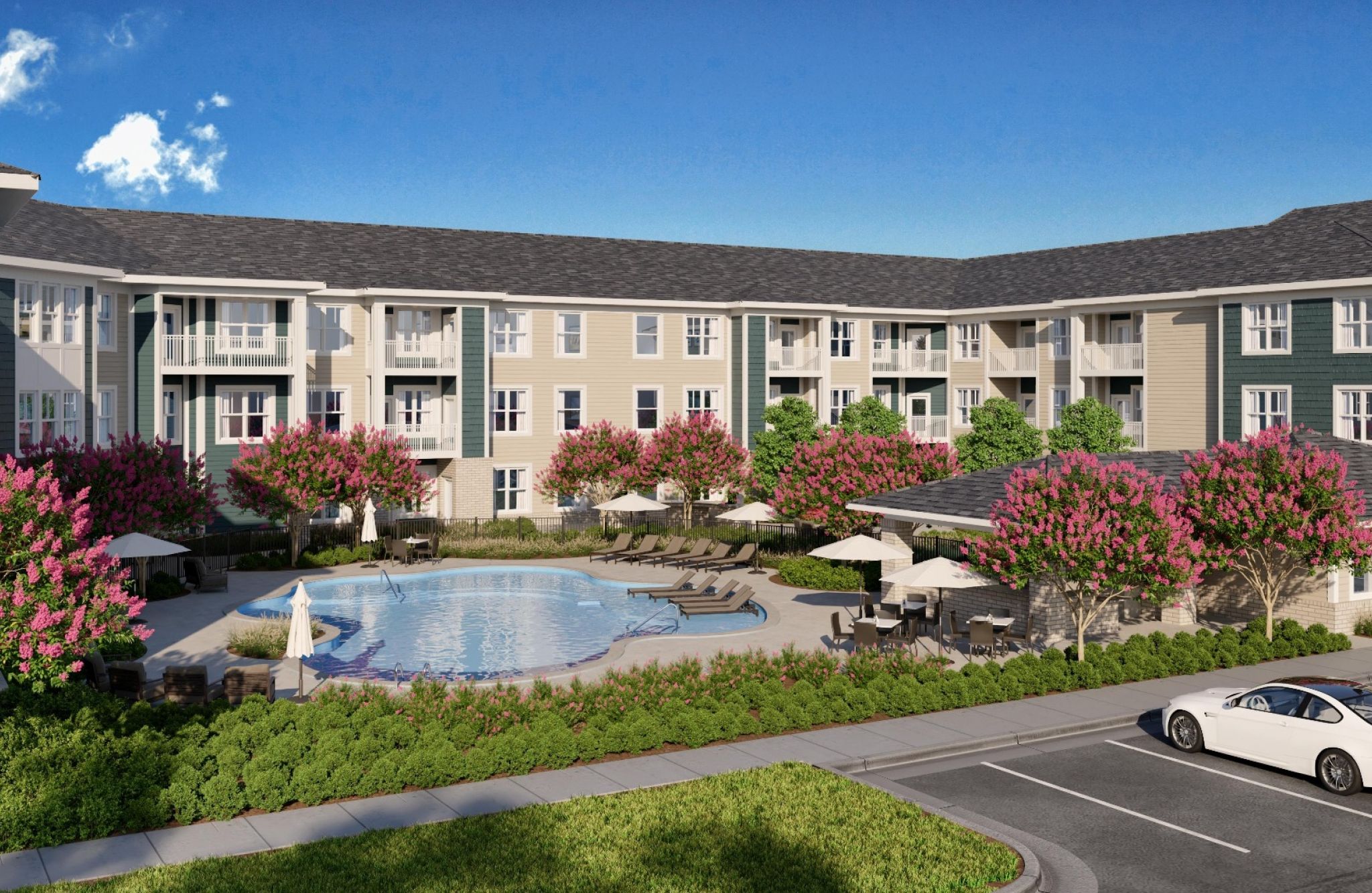 An apartment complex at Chics Beach, featuring a pool, pink-flowered trees, and a parking lot with a white car.