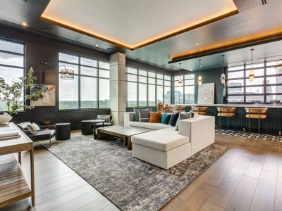 Modern lounge by Vest Residential with large windows, sectional sofa, bar area with stools, and stylish lighting on a hardwood floor.