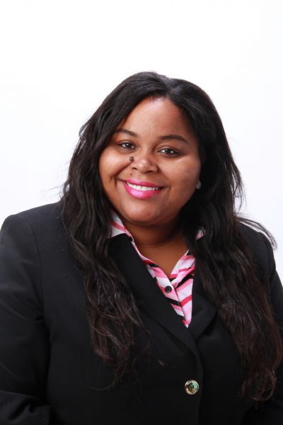 Aurelia Applewhite, in a black blazer and pink-striped shirt, smiles at the camera against a white background.