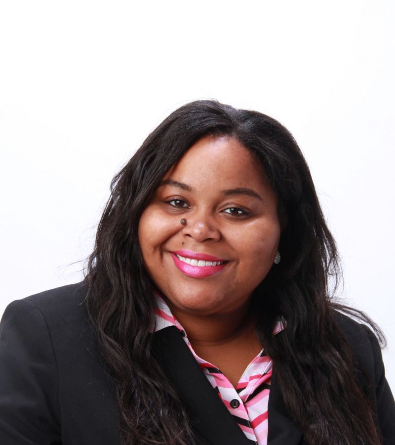 Aurelia Applewhite, in a black blazer and pink-striped shirt, smiles at the camera against a white background.