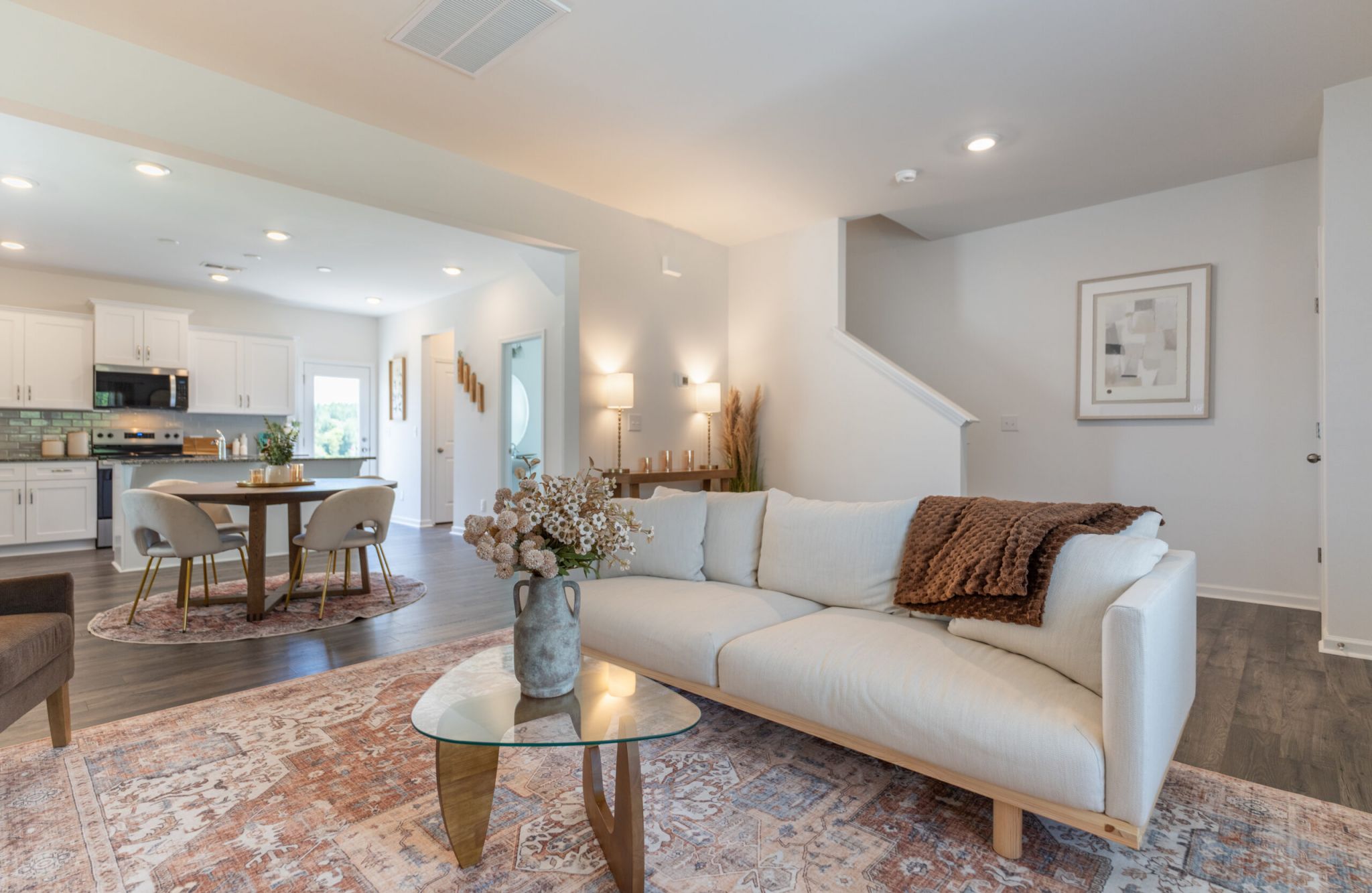 Bright living room at The Bend at Cramerton Mills with a white sofa, glass coffee table, and modern neutral decor open to kitchen and dining.