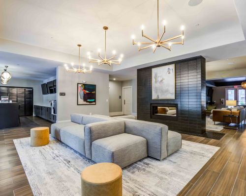Modern Woodside Eleven lounge with gray couches, chandeliers, artwork, and wooden flooring. Cozy ambiance enhanced by the fireplace.