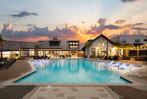 Outdoor pool area with loungers and modern buildings at sunset.