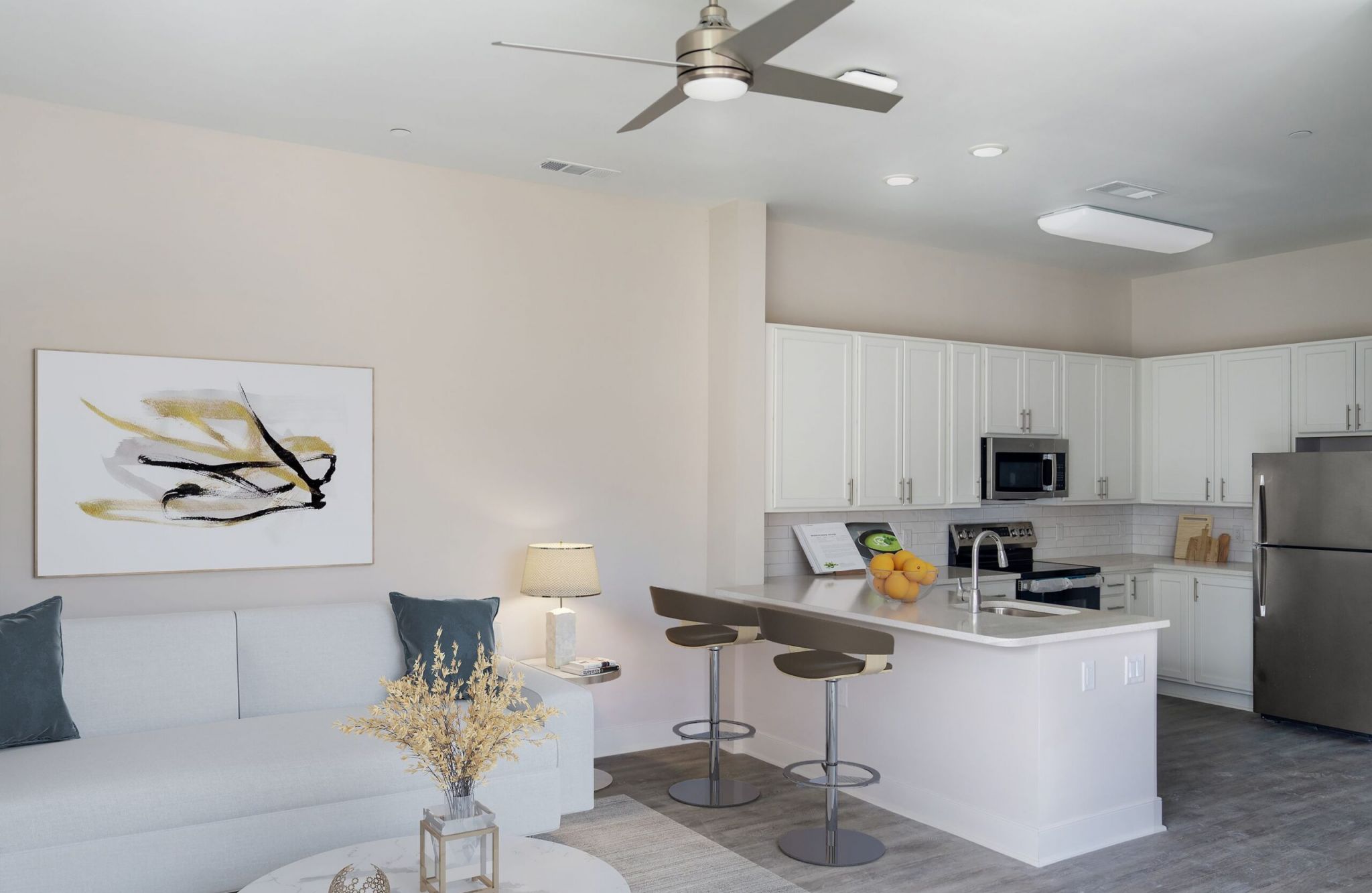 Modern kitchen and living room with white cabinets, gray accents, and abstract art on the wall; a space that truly earns acclaim.