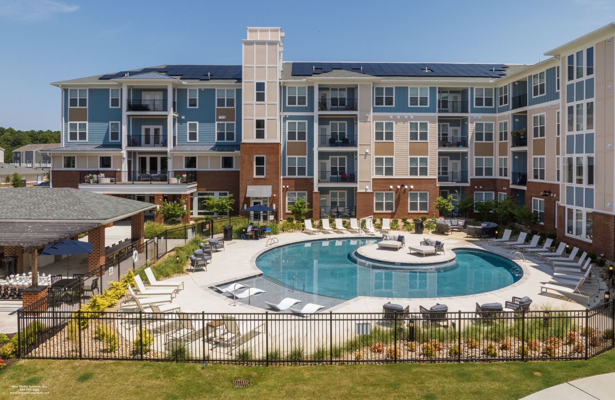 Apartment complex with a circular swimming pool and lounge chairs, offering an attainable sense of relaxation against a clear blue sky.