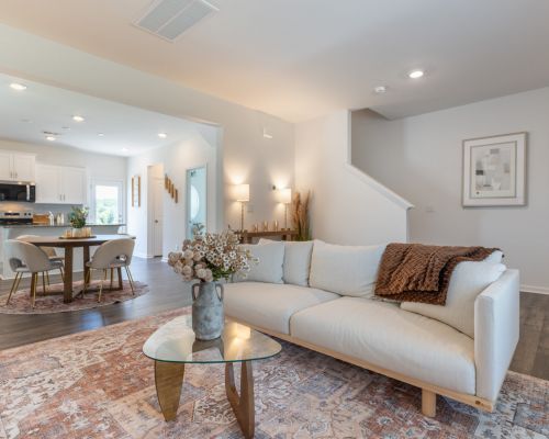 Bright living room at The Bend at Cramerton Mills with a white sofa, glass coffee table, and modern neutral decor open to kitchen and dining.