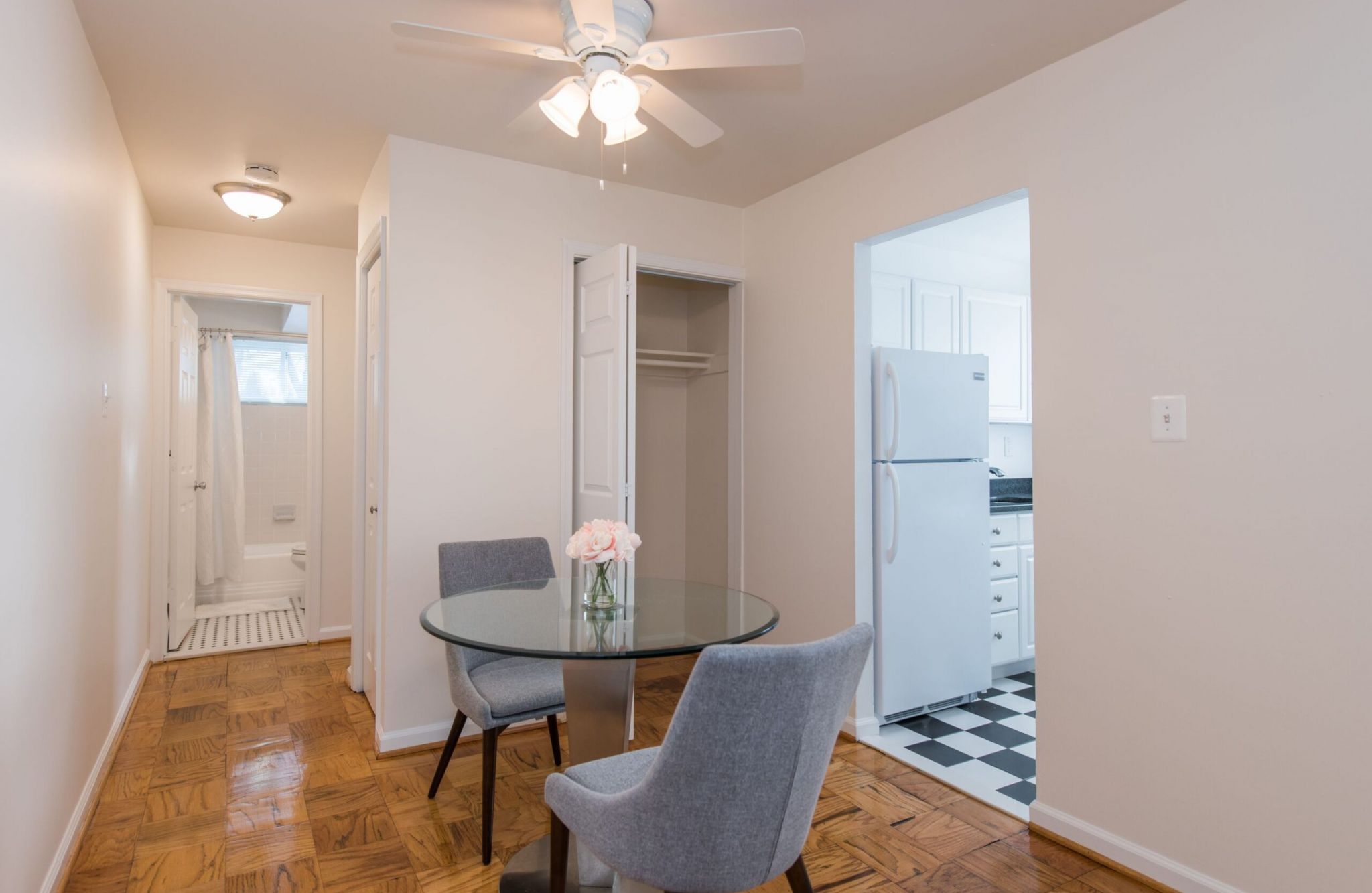 Cozy dining area with a glass table, two chairs, and views of the Mason Avenue Apartments' bathroom and kitchen entrances.