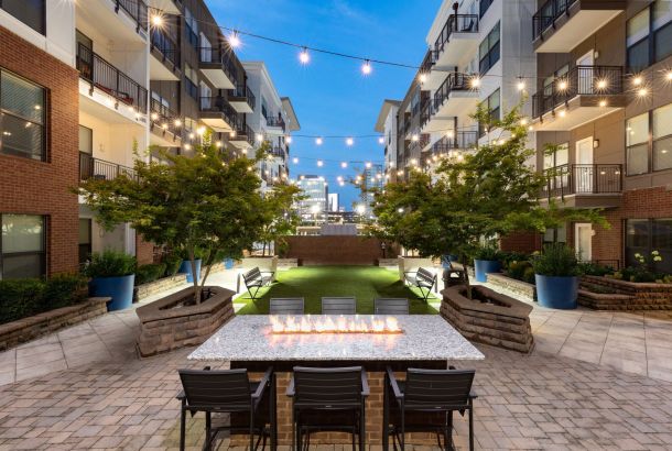 The modern courtyard at 1505 Demonbreun features string lights, a long fire pit table, and trees in planters.