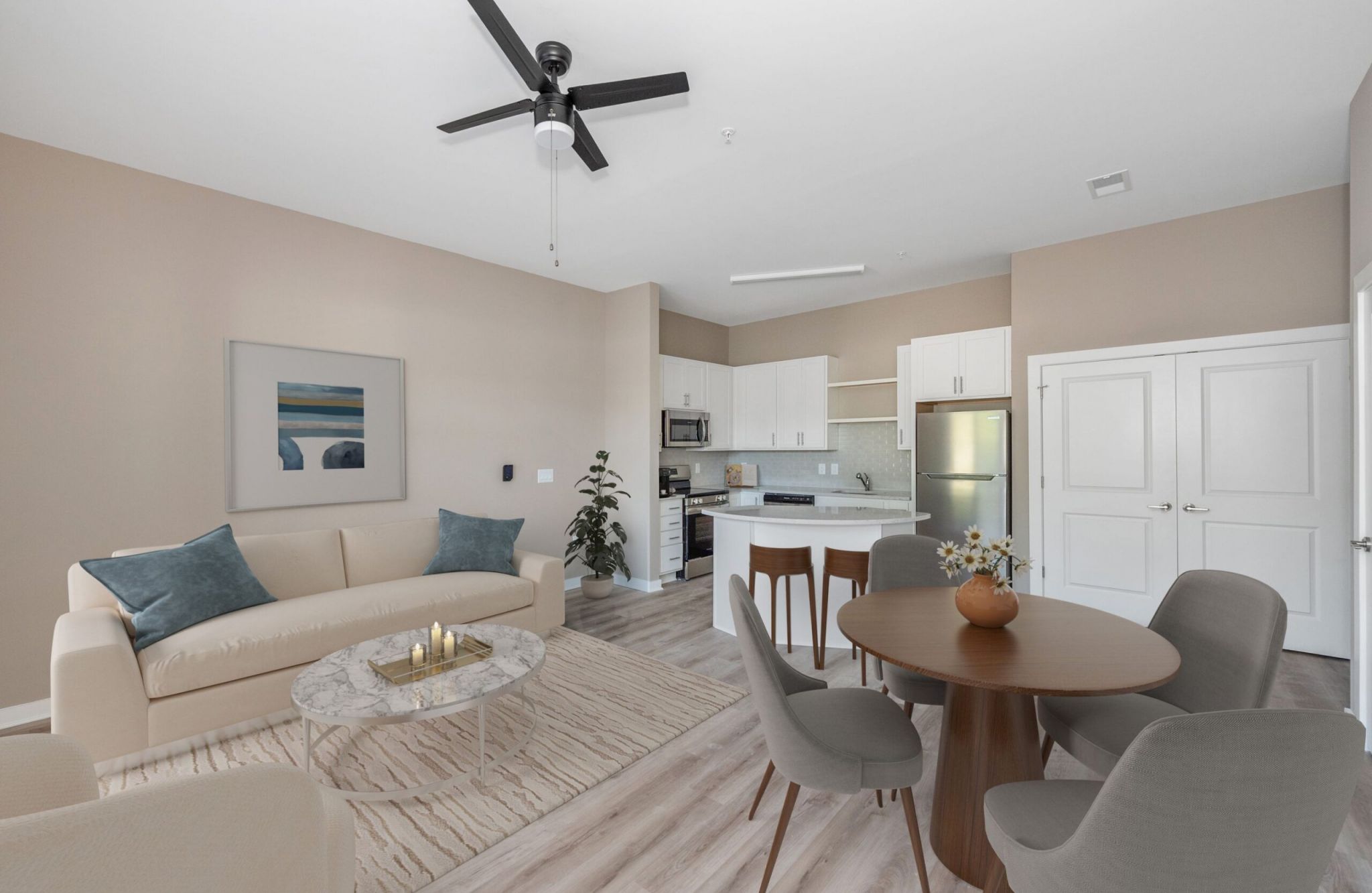 Modern open-concept living and dining area at Cary Pointe, featuring light wood flooring, beige walls, a sofa, and a kitchen with white cabinets.