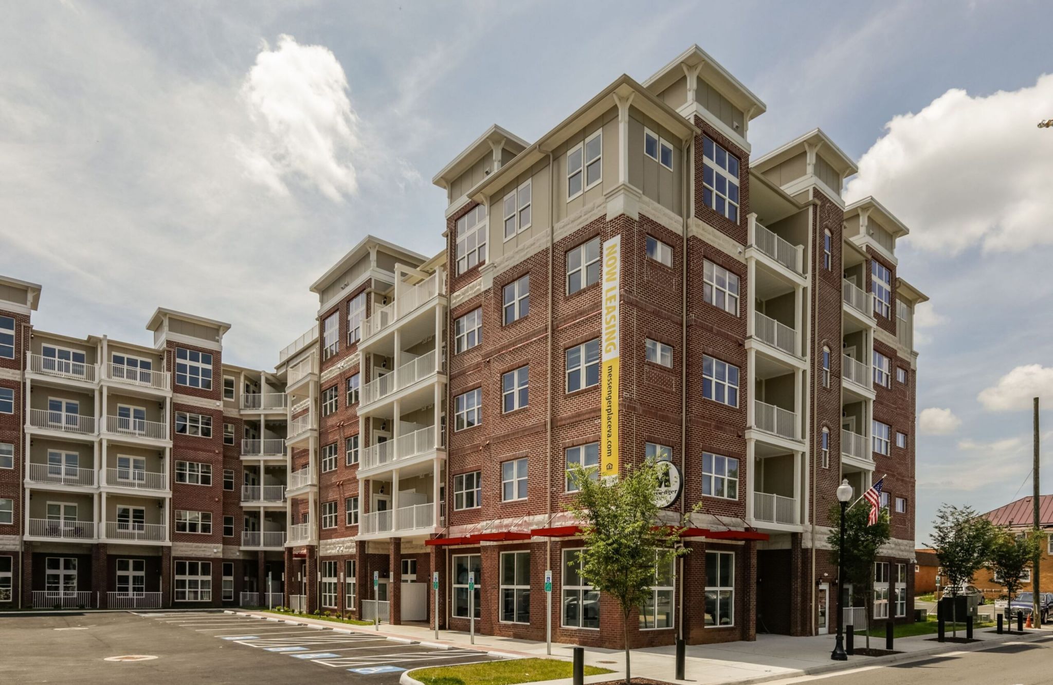 A modern brick apartment building with balconies and a parking lot, the perfect place to enjoy sunny days.