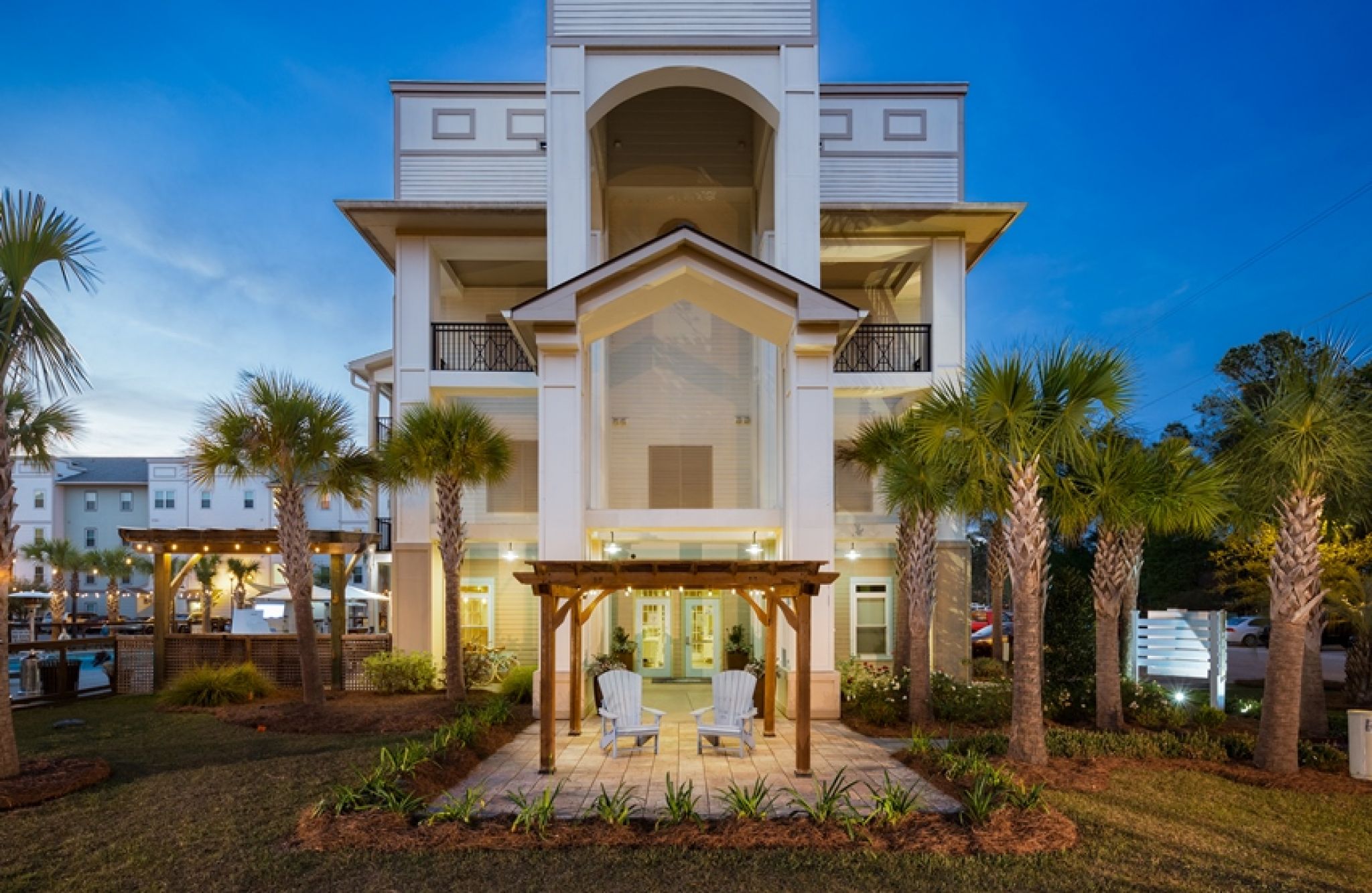 Modern house with palm trees and patio at dusk, featuring two white chairs under a wooden pergola—perfect for channel family evenings.
