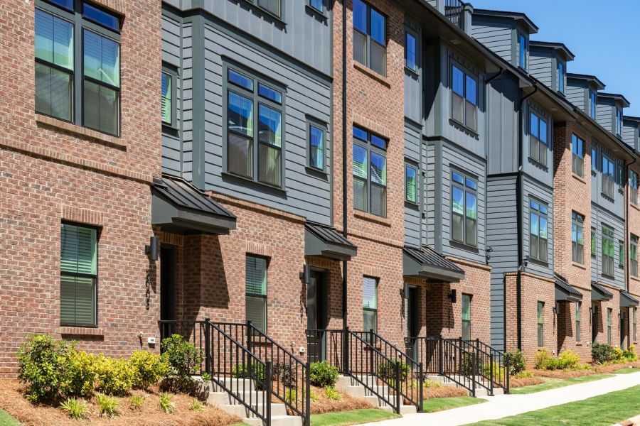 Modern brick and siding townhouses with black railings, large windows, and small landscaped front yards on a sunny day.