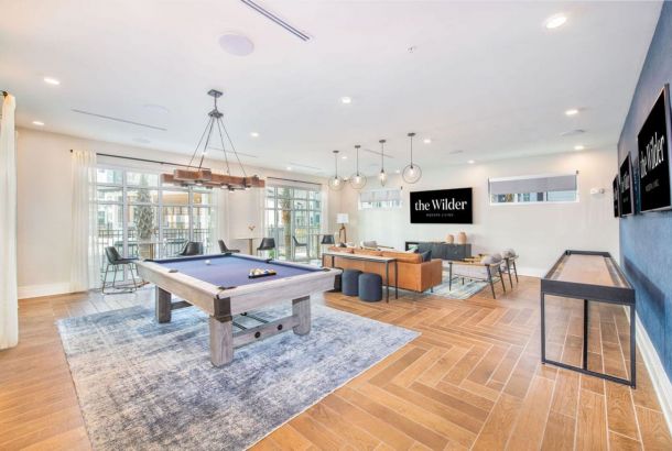 Modern recreation room with pool table, shuffleboard, and lounge area featuring a sign reading "the Wilder.