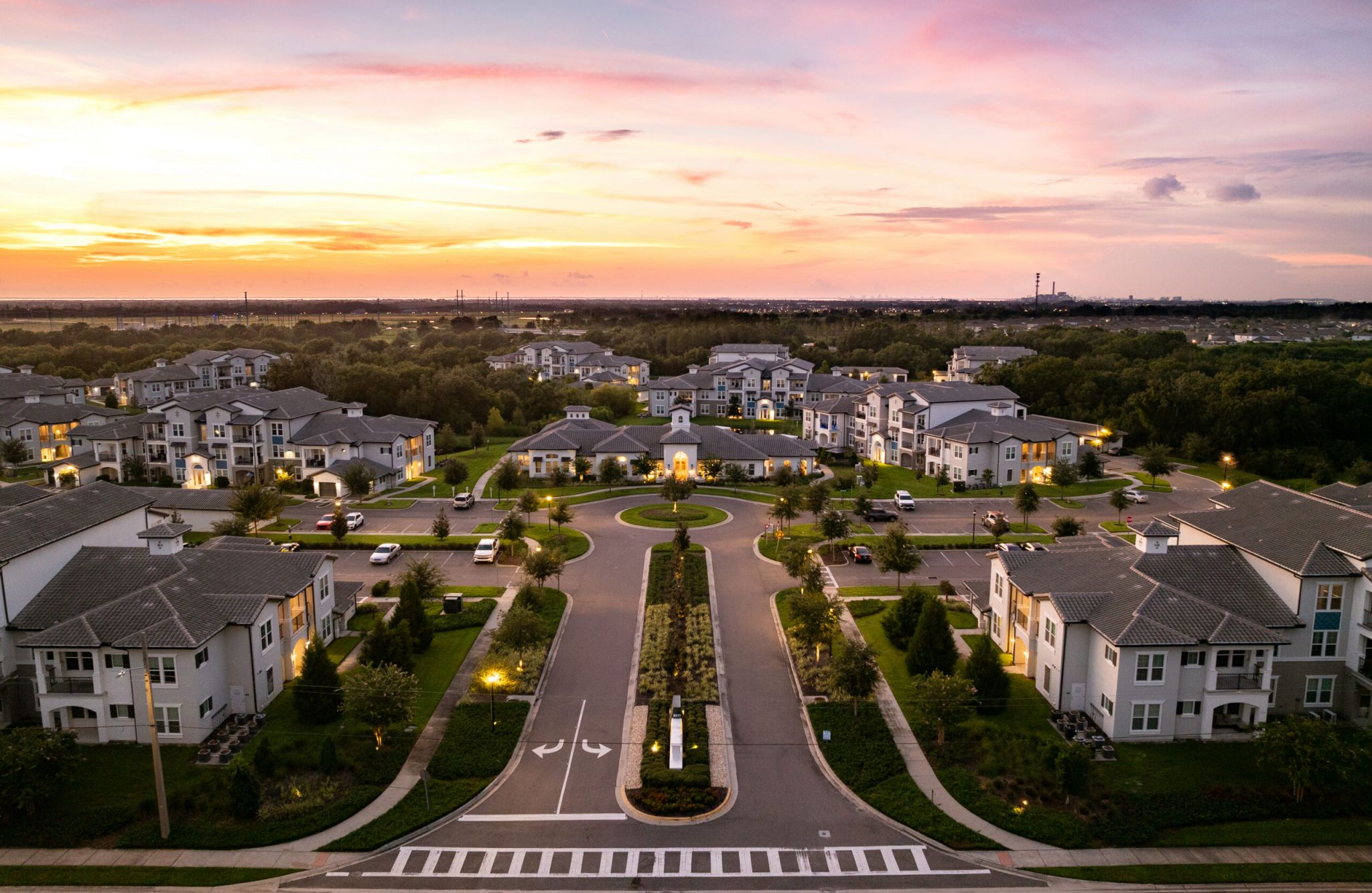 Aerial view of a suburban neighborhood with apartment buildings at sunset, surrounded by greenery and well-lit streets.
